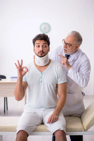 Genç boynu yaralı erkek hasta yaşlı erkek doktoru ziyaret ediyor. — Stok fotoğraf