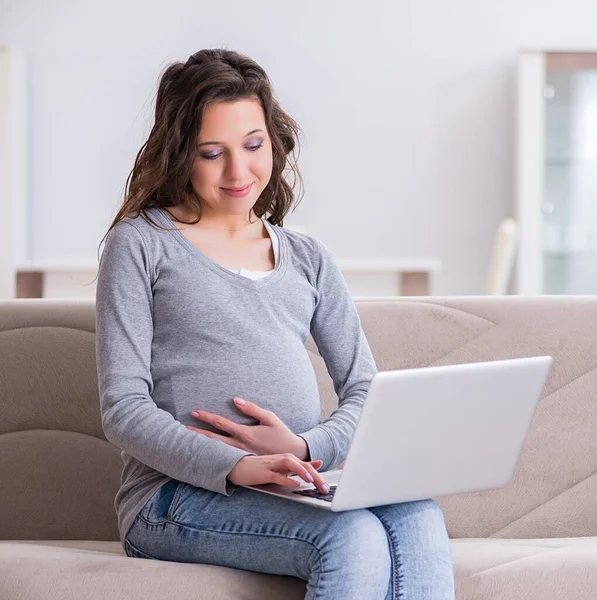 Mujer embarazada trabajando en el ordenador portátil sentado en el sofá — Foto de Stock