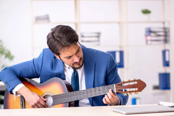 Giovane dipendente di sesso maschile che suona la chitarra sul posto di lavoro — Foto Stock