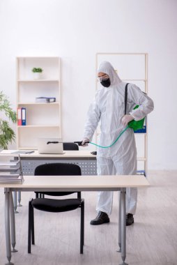 Young male contractor disinfecting office during pandemic