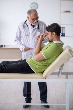 Genç erkek hasta yaşlı erkek doktoru ziyaret ediyor.