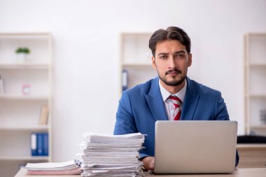 Genç bir erkek çalışan ve ofiste çok fazla iş var.