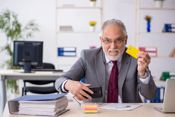 Old male employee holding credit card in the office — Stock Photo, Image