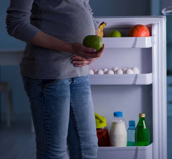 Mulher grávida perto de geladeira à procura de alimentos e lanches à noite — Fotografia de Stock