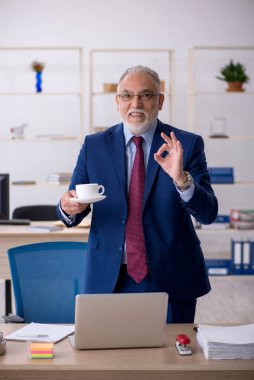 Eski erkek çalışan ofiste kahvaltı yapıyor.