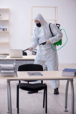 Young male contractor disinfecting office during pandemic