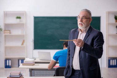 Yaşlı erkek öğretmen ve genç erkek öğrenci tahtanın önünde.