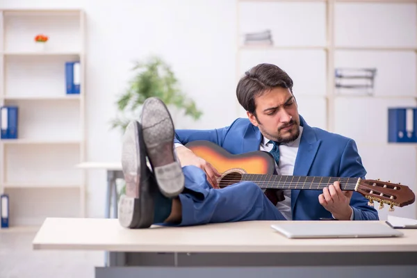 Joven empleado masculino tocando guitarra en el lugar de trabajo — Foto de Stock