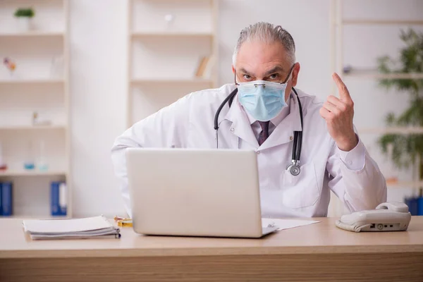 Vecchio medico maschio che lavora in clinica durante la pandemia — Foto Stock