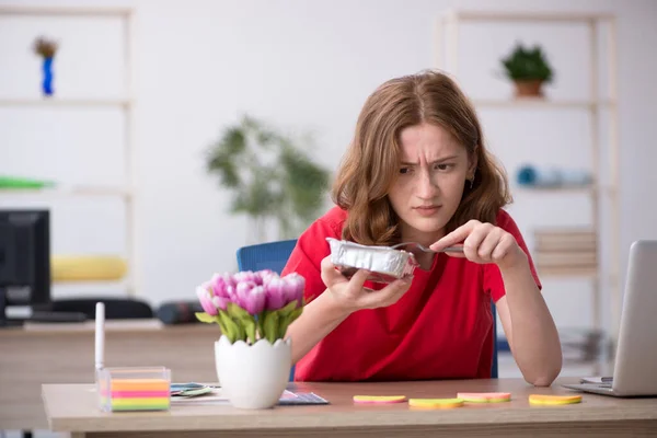 Ung kvinnelig designer spiser frokost på kontoret – stockfoto
