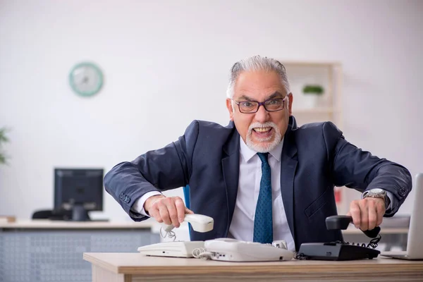 Viejo empleado hablando por teléfono en el lugar de trabajo — Foto de Stock