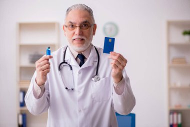 Yaşlı doktor kredi kartı tutuyor.