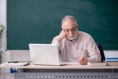 Tahtanın önünde yaşlı bir erkek öğretmen.