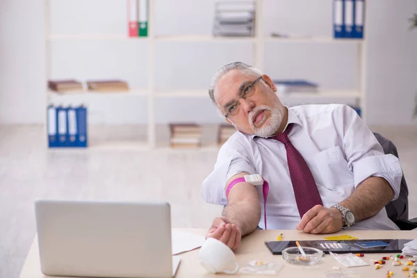 Vecchio dipendente tossicodipendente seduto in ufficio — Foto Stock