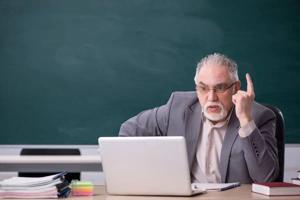 컴퓨터 컨셉트로 칠판 앞에 앉아 있는 늙은 남성 교사 — 스톡 사진
