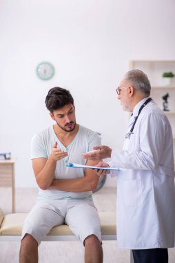Genç erkek hasta yaşlı erkek doktoru ziyaret ediyor.