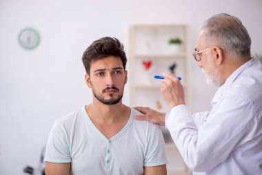 Genç erkek hasta yaşlı erkek doktoru ziyaret ediyor.