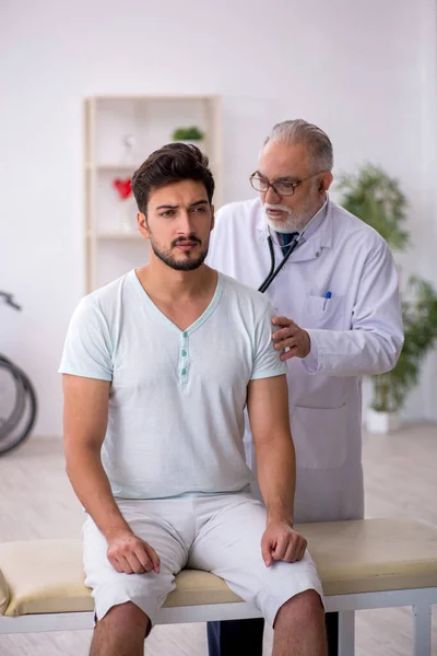Mladý pacient mužského pohlaví na návštěvě starého lékaře — Stock fotografie