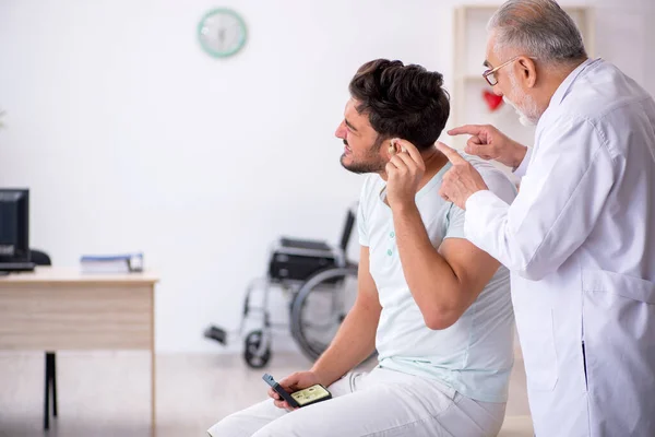 Jonge mannelijke patiënt met gehoorproblemen die oude arts otor bezoekt — Stockfoto