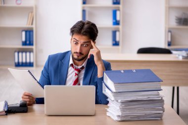 Genç bir erkek çalışan ve ofiste çok fazla iş var.
