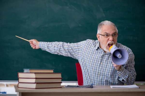 Old male teacher holding megaphone in the classroom — Stock Photo, Image