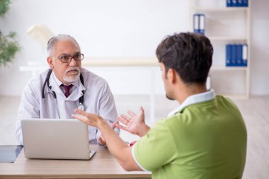 Genç erkek hasta yaşlı erkek doktoru ziyaret ediyor.