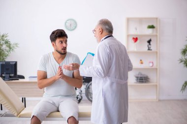 Genç erkek hasta yaşlı erkek doktoru ziyaret ediyor.