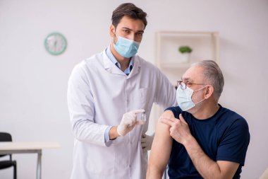 Yaşlı bir erkek hasta aşıyla genç bir doktoru ziyaret ediyor.