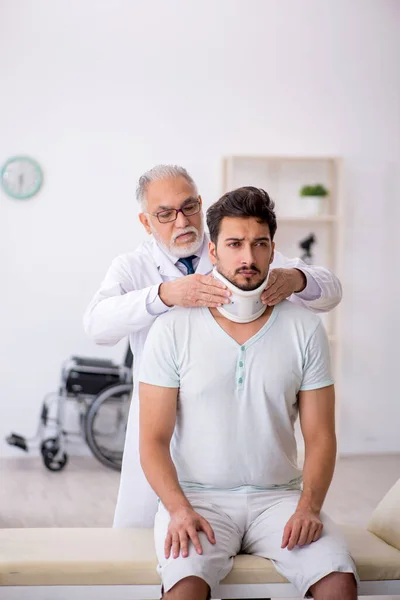 Genç boynu yaralı erkek hasta yaşlı erkek doktoru ziyaret ediyor. — Stok fotoğraf
