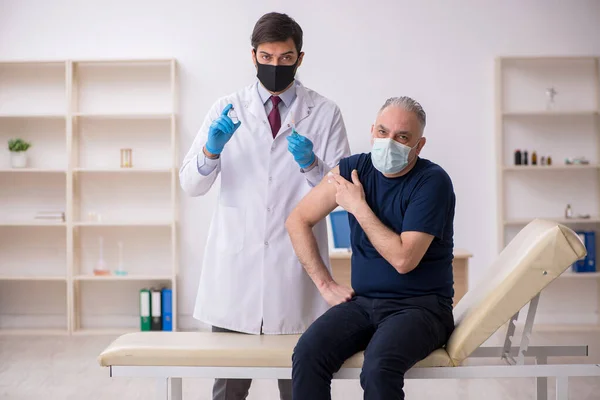 Alte männliche Patientin besucht jungen männlichen Arzt im Impfpass — Stockfoto
