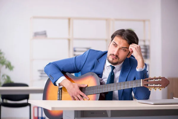 Jeune employé masculin jouant de la guitare sur le lieu de travail — Photo