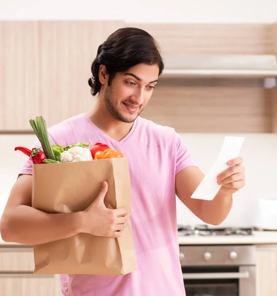 Den unga stilige mannen med grönsaker i köket — Stockfoto