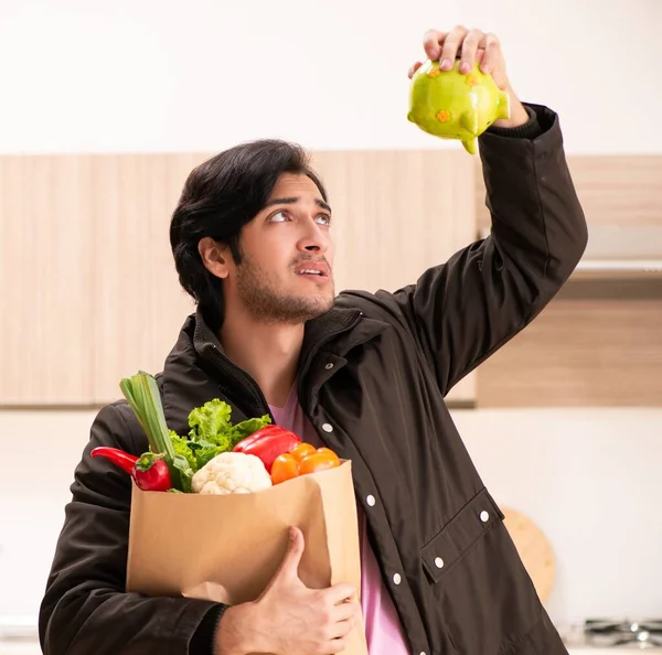 Den unga stilige mannen med grönsaker i köket — Stockfoto