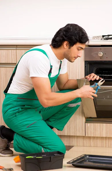 O empreiteiro jovem que repara o forno na cozinha — Fotografia de Stock