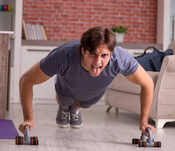 O jovem homem bonito fazendo exercícios esportivos em casa — Fotografia de Stock