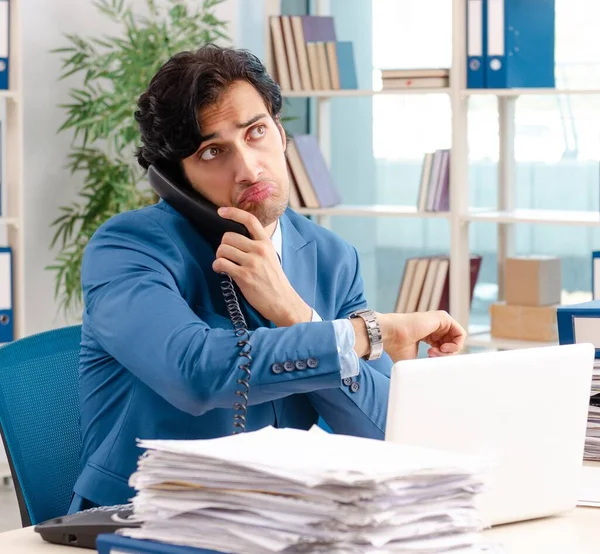 De jonge knappe mannelijke werknemer met te veel werk in het kantoor — Stockfoto