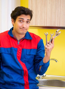 Tesisatçı mutfakta musluğu tamir ediyor.