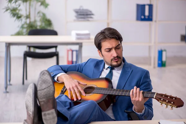 Giovane dipendente di sesso maschile che suona la chitarra sul posto di lavoro — Foto Stock