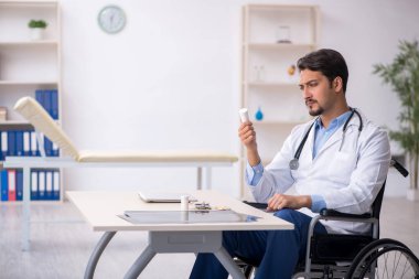 Klinikte çalışan tekerlekli sandalyedeki genç erkek doktor.