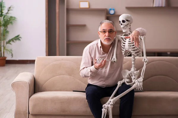 Старик сидит на диване с женским скелетом — стоковое фото