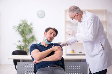 Genç erkek hasta yaşlı erkek doktoru aşıyla ziyaret ediyor.