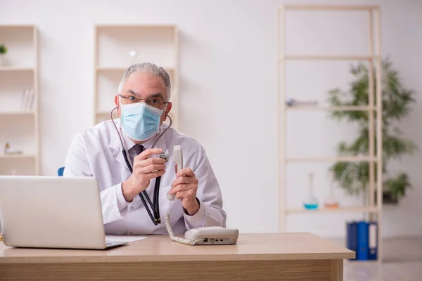 Oude mannelijke arts werkzaam in de kliniek tijdens pandemie — Stockfoto