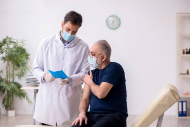 Yaşlı bir erkek hasta aşıyla genç bir doktoru ziyaret ediyor.