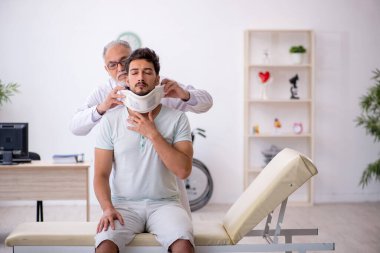 Genç boynu yaralı erkek hasta yaşlı erkek doktoru ziyaret ediyor.