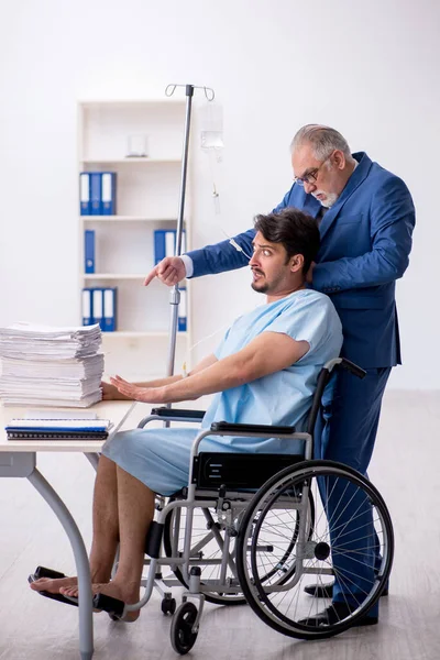 Jonge mannelijke werknemer in rolstoel voelt zich slecht op de werkplek — Stockfoto