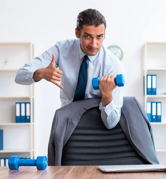 Joven empleado guapo haciendo ejercicios deportivos en el lugar de trabajo —  Fotos de Stock