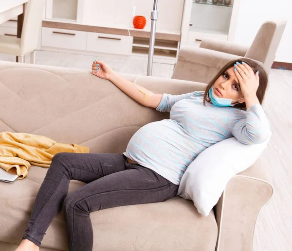 Den unga gravida kvinnan sitter i soffan hemma — Stockfoto