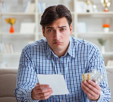 Kanepede ilaç ve reçeteyle oturan genç adam.