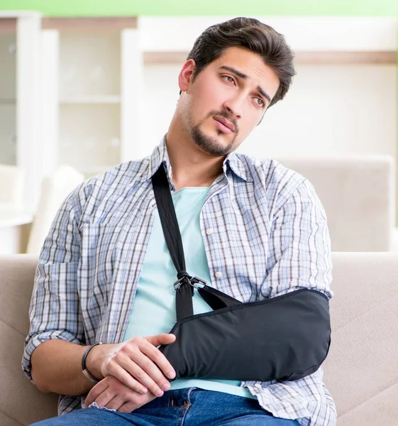 Молодой студент с травмой руки сидит на диване — стоковое фото