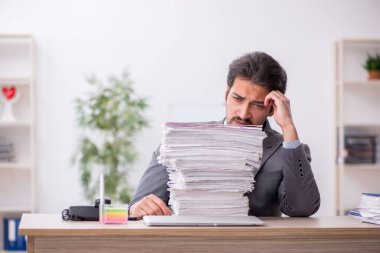 Genç bir erkek çalışan ve ofiste çok fazla iş var.